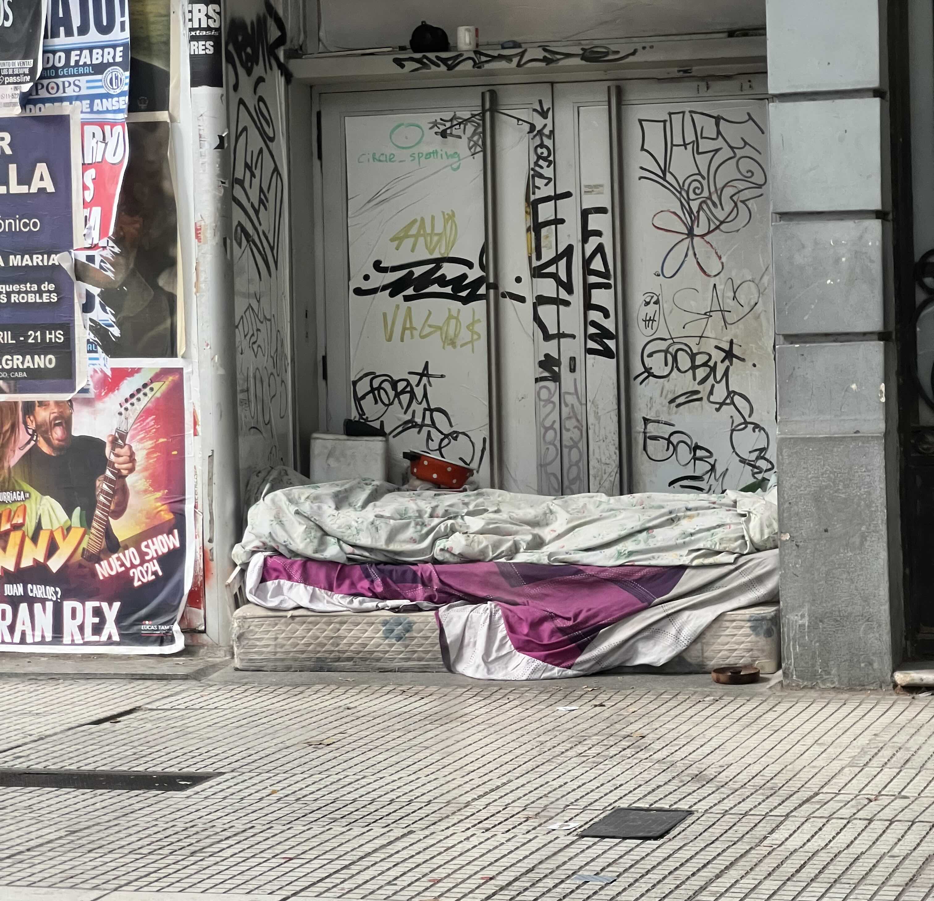 Makeshift bed on a graffiti-covered city sidewalk.