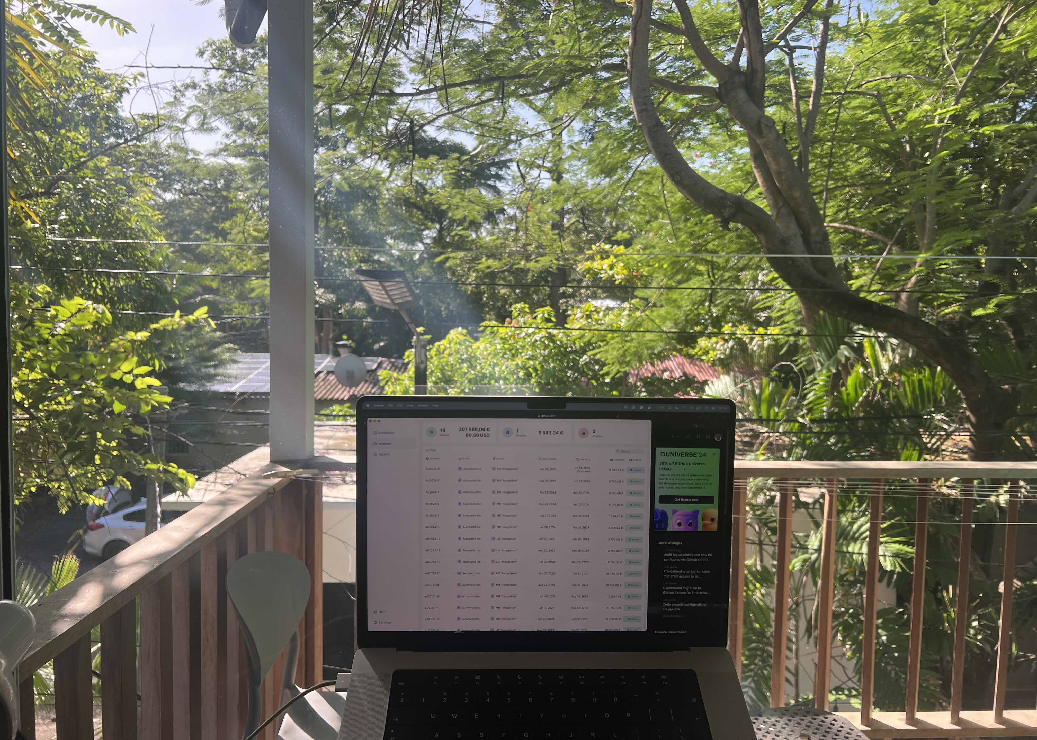 A laptop open on a table, set on a balcony overlooking lush greenery, capturing a moment of tranquility in the midst of El Tunco