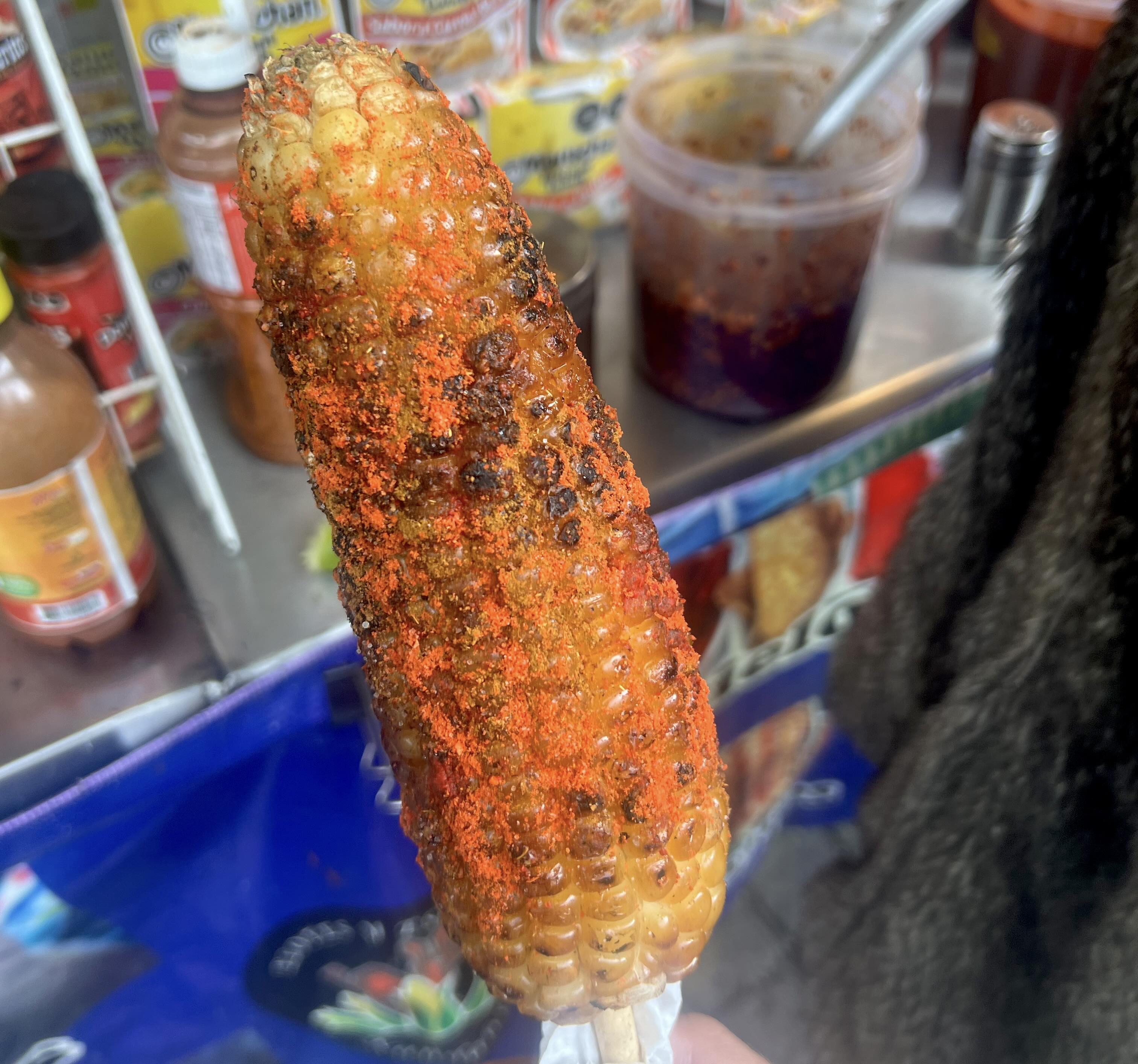 A close-up of grilled Mexican street corn on a stick, seasoned with chili powder and spices